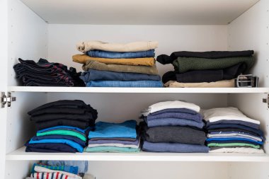 Dolabın içinde düzgünce istiflenmiş ve katlanmış renkli erkek kıyafetleri manzarası