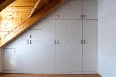 Eğri çatılı büyük bir yatak odasına inşa edilmiş özel yapım bir dolabın iç görünümü.