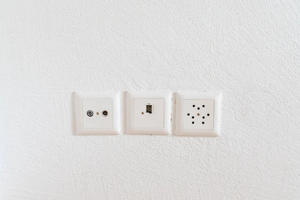 A close up view of sockets for television, internet, telephone and electricity on a white plaster wall