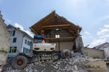 Terk edilmiş ev, ön planda gezici kazıcı, moloz ve kayalarla yıkıldı.
