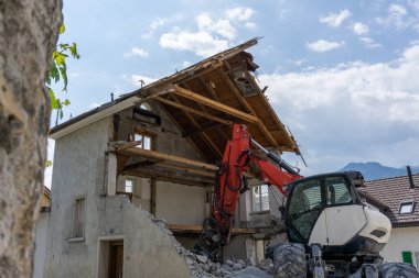 Terk edilmiş ev, ön planda gezici kazıcı, moloz ve kayalarla yıkıldı.