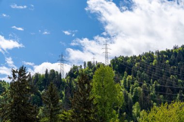 İsviçre Alplerinde yüksek voltajlı elektrik hatları ve kafes ormanı ve mavi gökyüzü altındaki dağları fotokopi alanı ile geçer.