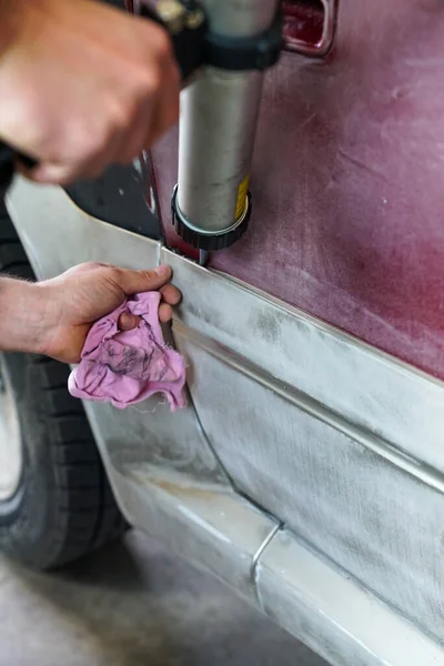 Male car mechanic using a pneumatic putty gun to glue car parts before a paint job in the body shop