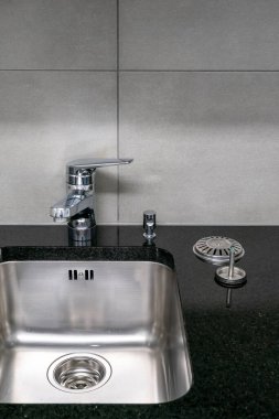 Çok temiz bir mutfak lavabosu, musluğu ve siyah kuvars taşı atölyesinin lazer ve lavabo tıkanıklığıyla yakın plan.