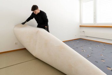 Bir tesis yönetimi şirketinin profesyonel temizleyicisi temizlik ve yenileme işi sırasında yatak odasındaki çirkin eski halıyı temizler.