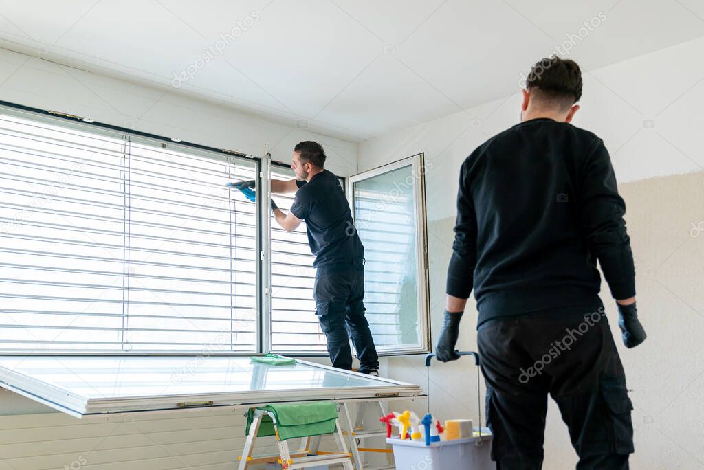A professional cleaning team in an apartment cleaning windows and blinds with a vacuum and other cleaning equipment