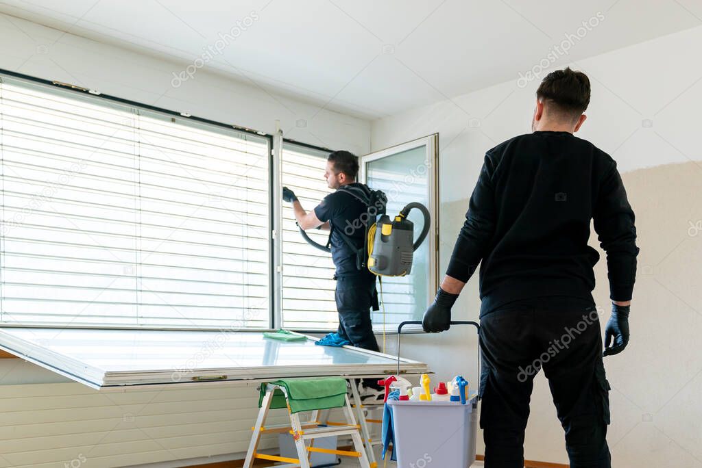 A professional cleaning team in an apartment cleaning windows and blinds with a vacuum and other cleaning equipment