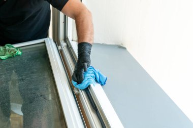 Kirli bir pencere çerçevesini mikro fiber bezle temizleyen profesyonel bir temizlikçi.