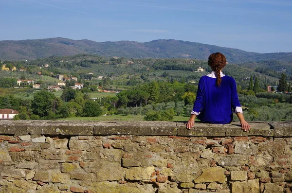 Young woman in blue shirt sitting on a stone wall looking at the — Stock Photo, Image