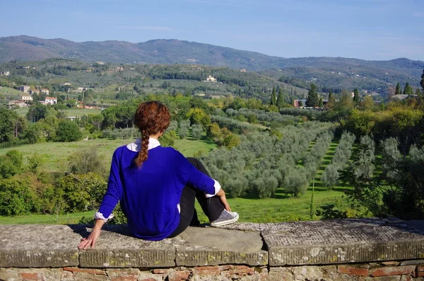 Junge Frau in blauem Hemd sitzt auf einer Steinmauer und blickt auf die — Stockfoto