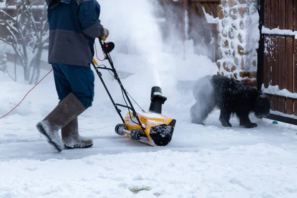 Adam evin bahçesinde kar temizleme makinesiyle kar temizliyor. Kar temizleyicisi çalışıyor. Karlı kış bahçesi.