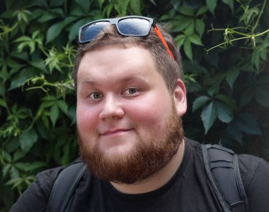 Young red bearded Man face.Fat smiling man with red beard. Green foliage background.