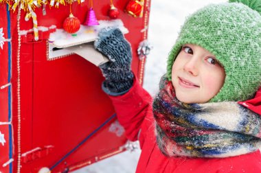 Sevimli mutlu çocuk kız Noel Baba 'ya mektup yolluyor. Noel 'e hazırlanıyorum ve Noel Baba' dan hediye sipariş ediyorum. Gülümseyen çocuk yılbaşı posta kutusunu attı.