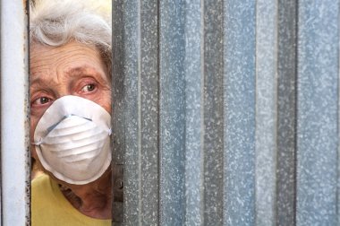 A frightened grandmother in a mask peeps out of the gap in the fence through the gate of her house. Isolation. Coronavirus covid-19. Quarantine elderly people. Stay home. Agoraphobia, mental disorder clipart