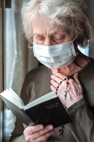 Пожилая Женщина Медицинской Респираторной Маске Возле Окна Молится Четками Крестом — стоковое фото