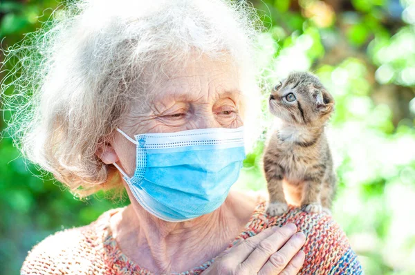 A cute elderly old woman in the garden holds a Scottish fold kitten on her shoulder. Quarantined, isolated. Coronavirus covid-19. Pets help old people cope with loneliness. Solitude. Pet care