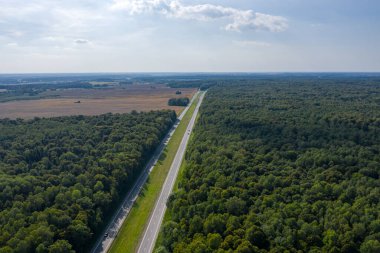 Uzağa giden uzun, düz, çift şeritli bir otoyol. Her iki tarafta bir orman ve bir tarla var. Bir İHA 'nın üstünden alındı..