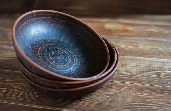 Handmade red clay clay plates lay on top of each other on a rough wooden table