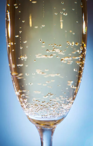 Champagne with bubbles in a glass on a blue background, close-up