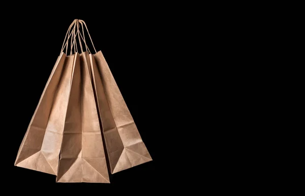 Three brown paper bags with cardboard handles on a black background. Copy space