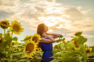 Gün batımında gökyüzüne karşı çiçek açan tarlada uzun saçlı güzel, genç ve zayıf bir kız.