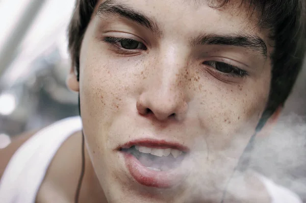 Genç bir adam ağzından sigara dumanı salıyor. Yakın plan.