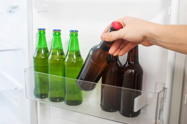 Erkek el buzdolabının kapısından bir şişe bira alır.