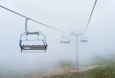 Dağlardaki açık bir kablodaki boş sandalyeler yoğun sis ve bulutlardan oluşan bir arka plana karşı.