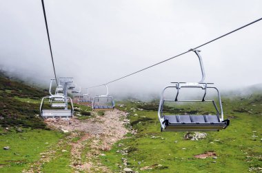 Dağlarda, yoğun sis ve bulutlardan oluşan bir arka planda açık bir kabloda bir sürü boş sandalye.