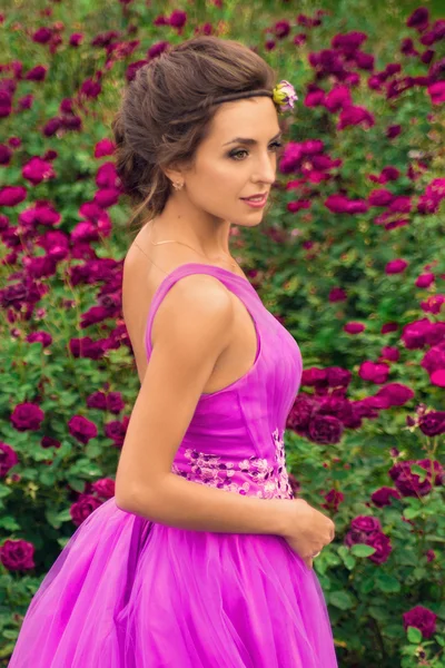 Vacker flicka i rosa bollen klänning bland blommorna i trädgården — Stockfoto