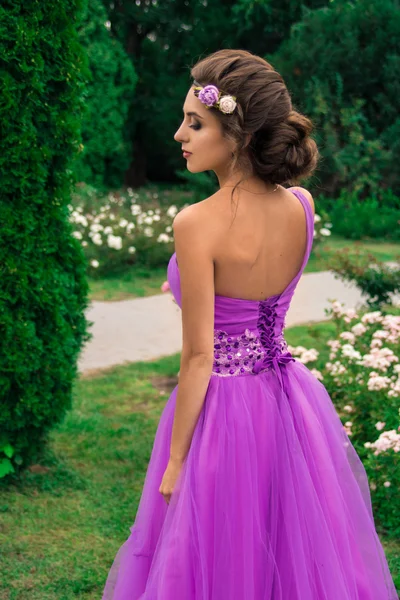 Vacker flicka i violett klänning bland i trädgården — Stockfoto