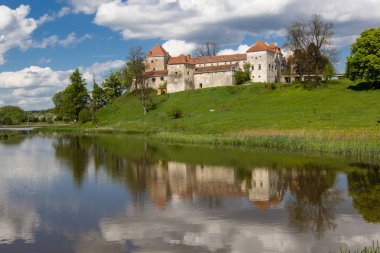 Etkileyici gökyüzü arka plan ile göl yakınlarındaki yeşil tepe üzerinde eski kale