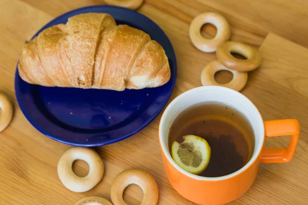 Кружка с черным чаем с лимоном, круассаном на тарелке и маленькими бубликами — стоковое фото