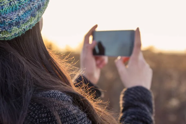 Молода дівчина тримає мобільний телефон під час заходу сонця на відкритому повітрі Стокове Зображення