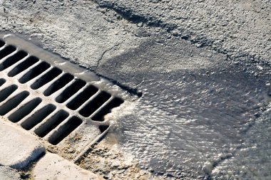 Aşağı su akıyor bir güneşli bahar gününde kanalizasyon kapağı