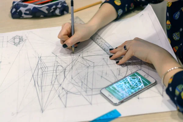 Girl architect draws a plan, design, geometric shapes by pencil on large sheet of paper at office desk. — Stock Photo, Image