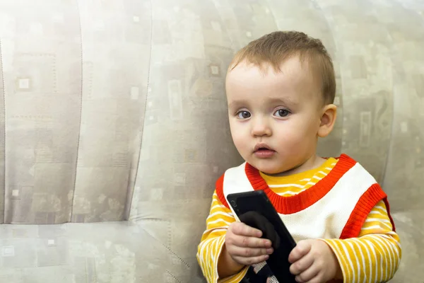 Ein kleiner Junge schaut auf das Smartphone, das auf der Couch liegt — Stockfoto