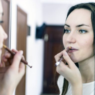 Genç kadın ofiste bir ayna önünde ruj uygulama