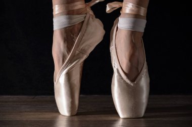 Yakın çekim klasik balerin'ın bacakları pointes siyah arka plan ve ahşap gri zemin içinde.