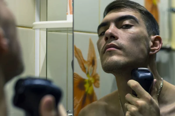 Reflection of young man in mirror shaving with electric shaver — Stock Photo, Image
