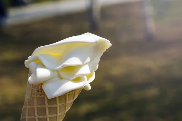 Cone de waffle com sorvete cremoso ao sol em um fundo de grama verde — Fotografia de Stock