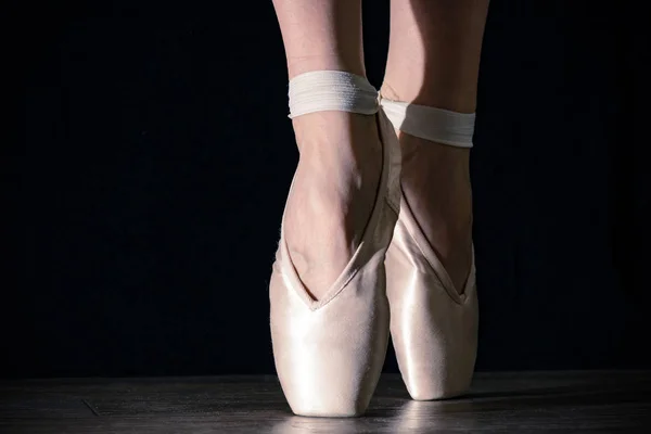 Close-up classic ballerina's legs in pointes on the black background and wooden grey floor. — Stock Photo, Image