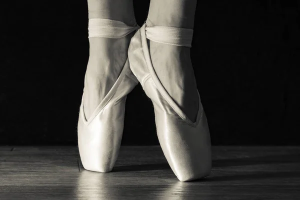 Close-up klassieke ballerina's benen in de pointes kunnen teweegbrengen op de zwarte achtergrond en een houten grijze vloer. — Stockfoto