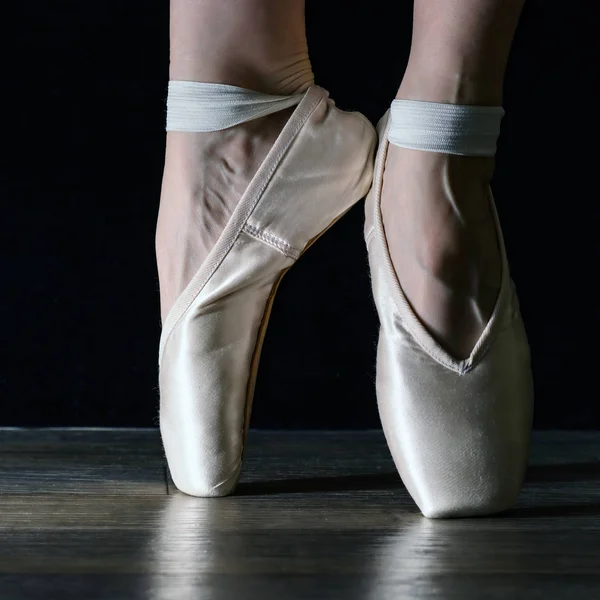 Patas de bailarina clásica de primer plano en puntas sobre fondo negro y suelo gris madera . —  Fotos de Stock