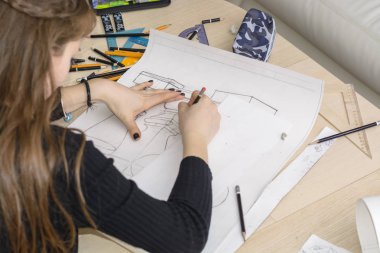 Kadın mimar bir plan çizer, tasarım, geometrik şekiller ofis masasındaki büyük kağıt üzerine kurşun kalemle çizer..