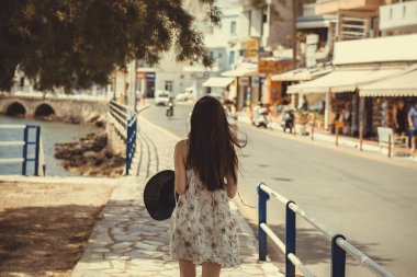 Genç bir kızın elinde siyah şapkalı Rethymno şehir, Yunanistan iskele yürür. Hasır Şapkalı boyunca yürüyen bir genç kız. Arkadan görüntülemek