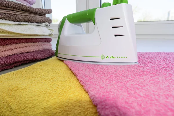 Ironing linen with iron. A stack of ironed towels lying next to the iron. Hot iron on an Ironing Board. Teflon sole plate covered with small holes