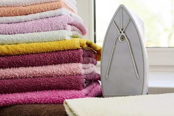 Ironing linen with steam generator. A stack of ironed towels lying next to the iron. Teflon sole plate covered with small holes