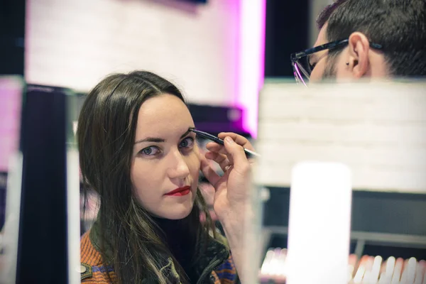 Mooie brunette met rode lippenstift is het testen van de eyeshadows in schoonheid winkel — Stockfoto