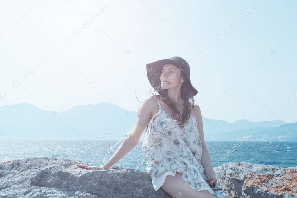 Outdoor summer portrait of young pretty woman looking to the camera in the port of Agios Nikolaos, enjoy her freedom and fresh air, wearing stylish hat and clothes